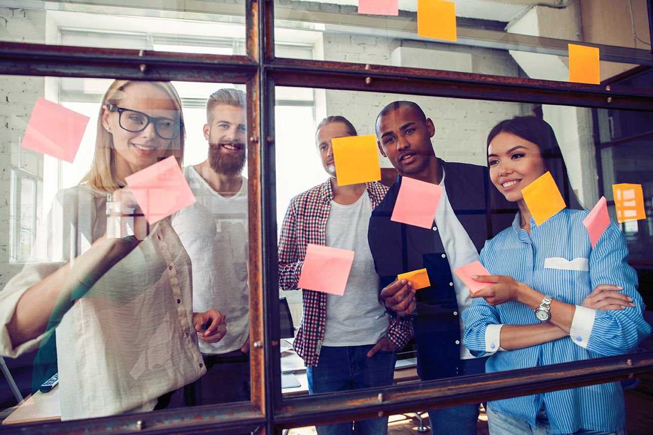 Business team looking at sticky notes on glass wall